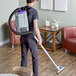 A man using a ProTeam backpack vacuum to clean a wood floor.