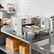A stainless steel countertop ventless impinger electric conveyor oven with a digital control panel and a 50-inch belt, shown in a commercial kitchen setting.