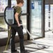 A woman using a ProTeam backpack vacuum to clean a carpet in a store aisle.