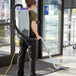 A woman using a ProTeam backpack vacuum to clean a carpet in a corporate office cafeteria.