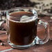 A Libbey glass mug filled with brown liquid and coffee beans.