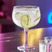 An Acopa gin and tonic glass filled with a drink and lime slices on a table with shot glasses.