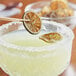 Dried key lime slices on a wooden stick garnishing a cocktail.