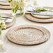 A table set with Acopa blond rattan charger plates, white plates, and white flowers.