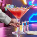 A bartender holding an Acopa Colossal martini glass with a red drink.