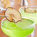 A pair of glasses with green liquid and a dried red apple slice on the rim.