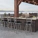 Holland Bar Stool stainless steel counter stool with black cushion at a counter in an outdoor patio.