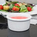 A white Tuxton china ramekin filled with pink liquid on a table with salad plates.