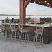 A Holland Bar Stool stainless steel slat back counter stool with a Breeze Champagne seat next to an outdoor counter.