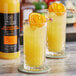 Two glasses of Twisted Alchemy Valencia orange juice with orange slices on top.