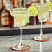 Two glasses of a yellow drink with Twisted Alchemy Persian Lime Juice and lime wedges on the side.