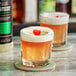 Two glasses of Twisted Alchemy lime sour cocktails with cherries on a coaster.
