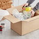 A person putting a can of food in a Lavex cardboard shipping box.