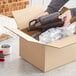 A person holding a bottle of beer in a Lavex heavy-duty cardboard shipping box.