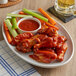 A plate of French's BBQ chicken wings with celery and carrots and a bowl of BBQ sauce.