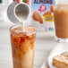 A person pouring Silk Unsweetened Almond Milk into a glass of iced tea.