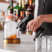 A person using a Flavour Blaster Rhubarb Cocktail Aroma device to add smoke to a glass with a drink in it.