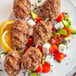 A plate of meat skewers with tomatoes and cucumbers on a white surface.