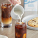 A person pouring Silk vanilla soy milk into a glass of iced coffee.