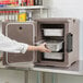 A woman opening a Cambro front-loading insulated food pan carrier in a professional kitchen.