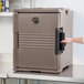 A person opening a brown Cambro Ultra Pan Carrier food container with black handles.