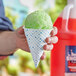 A hand holding a green paper cone filled with ice cream.