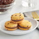 Three macarons on a white plate with chocolate chips next to a bowl of Valrhona Caraibe dark chocolate.