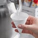 A hand using a Choice white paper cone to pour water into a cup.