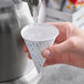 A hand holding a Choice paper cone cup with water pouring out of it.