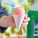 A hand holding a Choice white paper cone filled with pink snow cone.