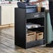 A man using a Lancaster Table & Seating black cash register stand with a locking drawer.