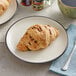 A plate with a chocolate hazelnut croissant and a cup of coffee on a table.