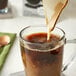 A spoon pouring Oatly Barista Edition oat milk into a glass cup.