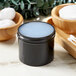 A black container with a white lid filled with white substance next to a bowl of cotton swabs.