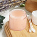 A clear plastic jar of pink scrub on a wooden surface.