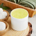 A white customizable jar of scrub on a wood surface next to a bowl of cotton.