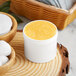 A white container of yellow cream next to a bowl of cotton balls.