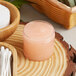 A clear jar of pink scrub on a wood surface.