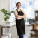 A woman in a black Choice Customization bib apron stands in a farm-to-table restaurant.