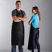 A man and woman wearing Choice black vinyl aprons in a professional kitchen.