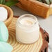 A clear straight sided glass jar of face cream on a wood surface.