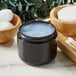 A black jar of blue gel next to a bowl of cotton buds and a wooden bowl.