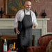 A man wearing a Choice black bib apron holding a glass of wine.