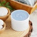 A white jar of blue cream on a wood surface.
