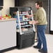 A man standing next to an Avantco black vertical air curtain merchandiser taking a package of food.