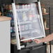 A man opening an Avantco black vertical air curtain merchandiser in a hospital cafeteria.