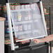 A woman pointing at a black Avantco vertical air curtain merchandiser.