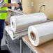 A person in a yellow vest using a machine to roll Lavex Pro 20" Polyolefin Shrink Film.