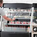 A man standing in front of a black Avantco vertical air curtain merchandiser.