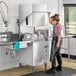 A woman in overalls stands in a professional kitchen next to a Ecoline by Hobart door-type dishwasher.